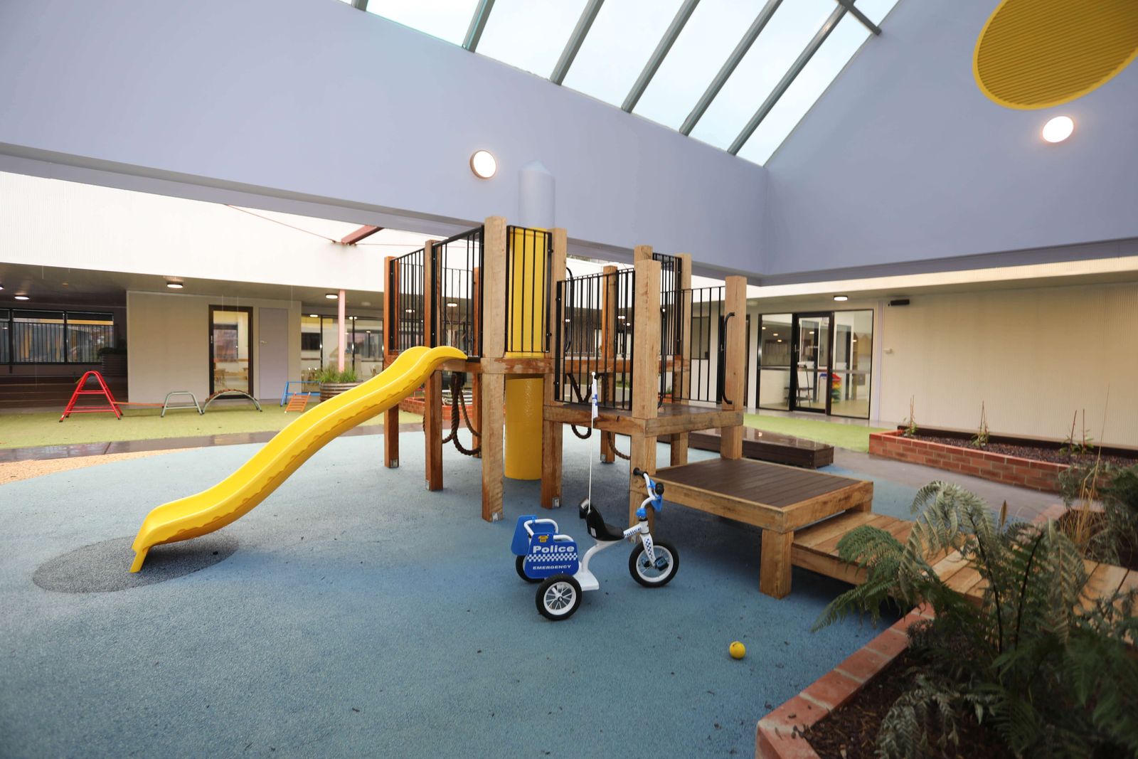 The courtyard playground with a timber fort, yellow slide and soft blue play surface