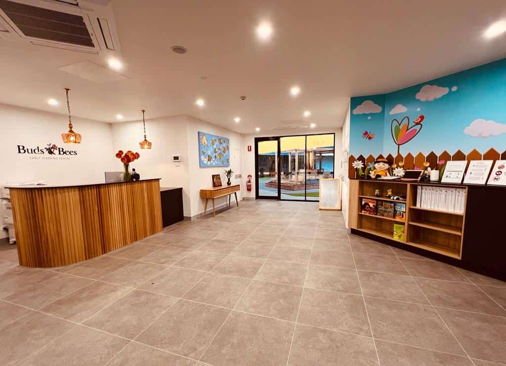 The Buds & Bees reception area with a timber desk, a bee and cloud mural and a view through to the courtyard