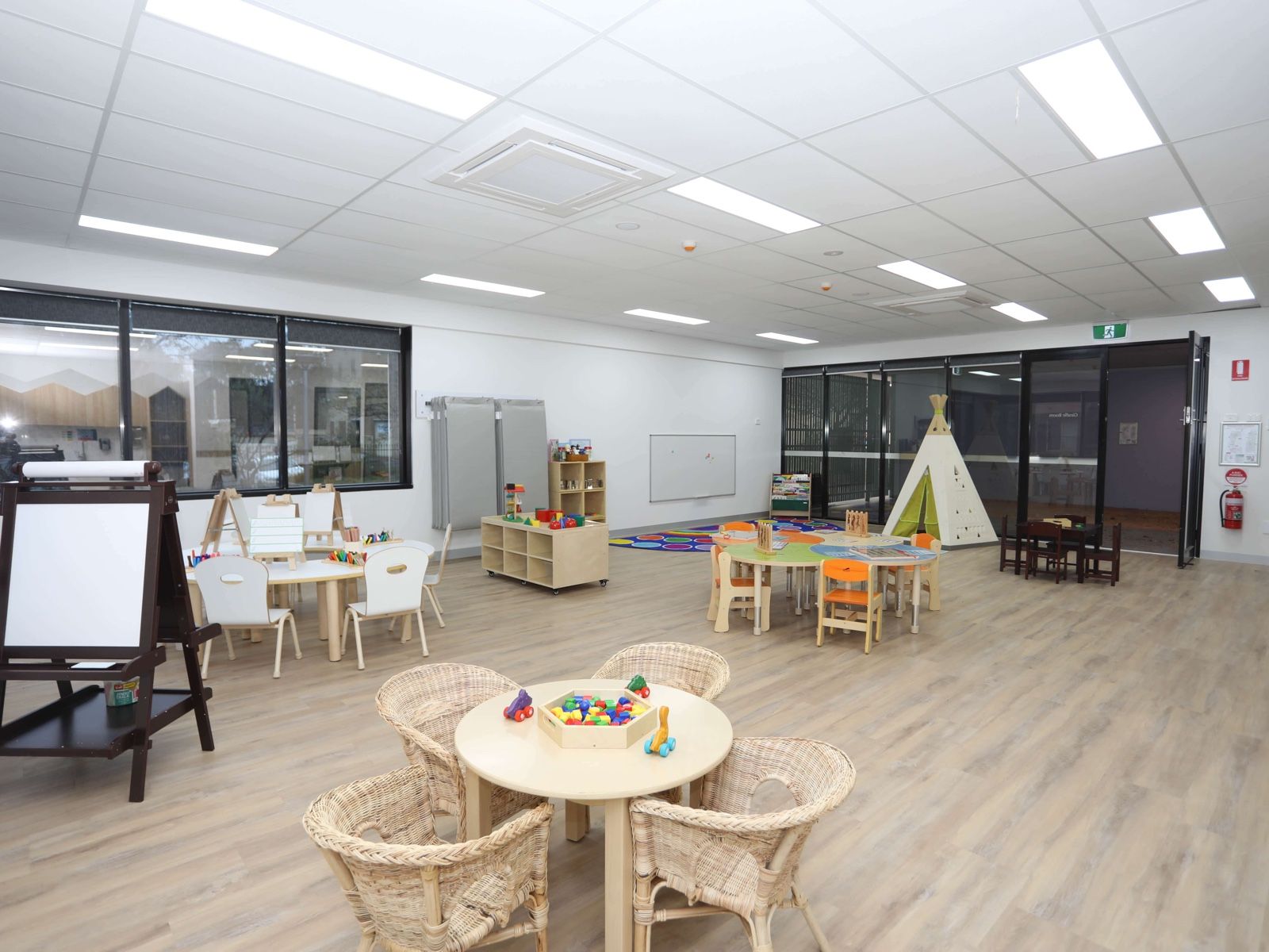 A light-filled room with an easel, cane chairs, small tables and a teepee
